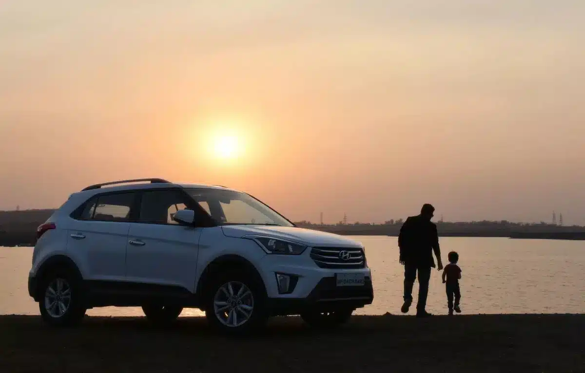 A white SUV parked by a lake at sunset with a man and child walking nearby.