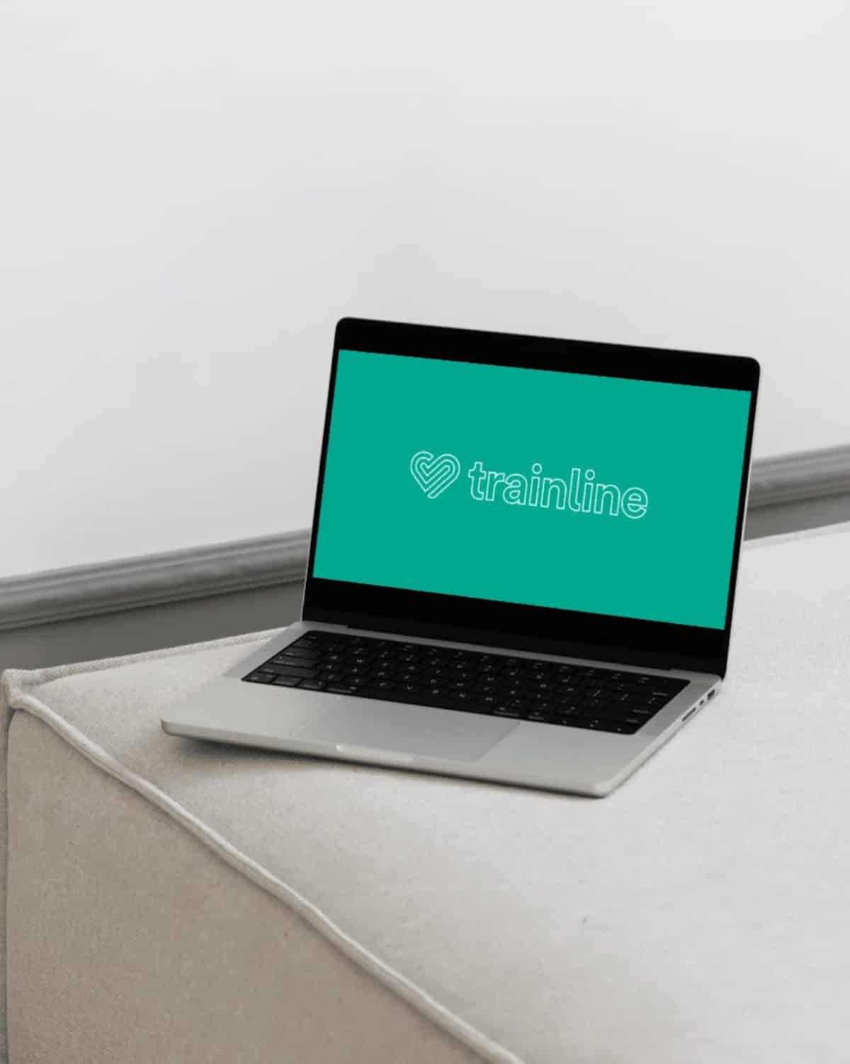 A laptop on a cushioned surface displays the Trainline logo on its screen.
